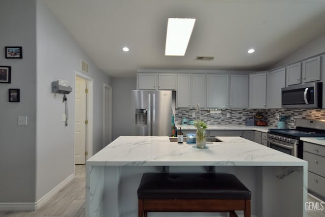 kitchen featuring gray cabinetry, a center island, backsplash, light stone counters, and stainless steel appliances