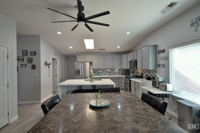 kitchen featuring gray cabinetry, a breakfast bar, lofted ceiling, a kitchen island, and stainless steel appliances