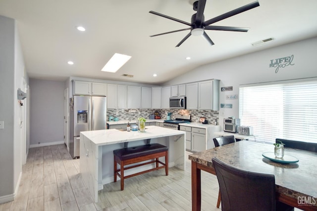 11712 Novara Ave, Bakersfield, CA 93312 - kitchen featuring appliances with stainless steel finishes, backsplash, a kitchen breakfast bar, a center island, and light wood finished floors
