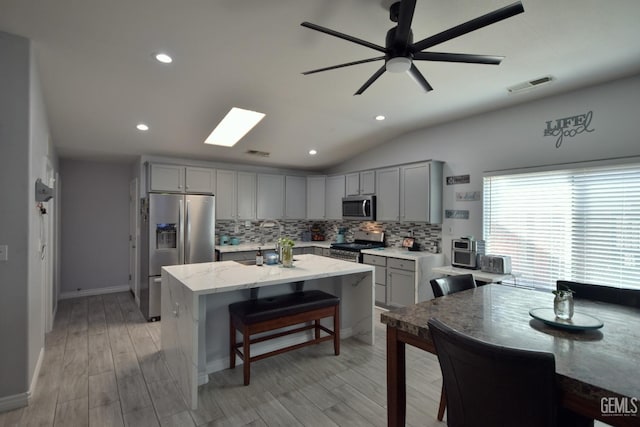 kitchen featuring gray cabinetry, light stone countertops, tasteful backsplash, light hardwood / wood-style floors, and stainless steel appliances