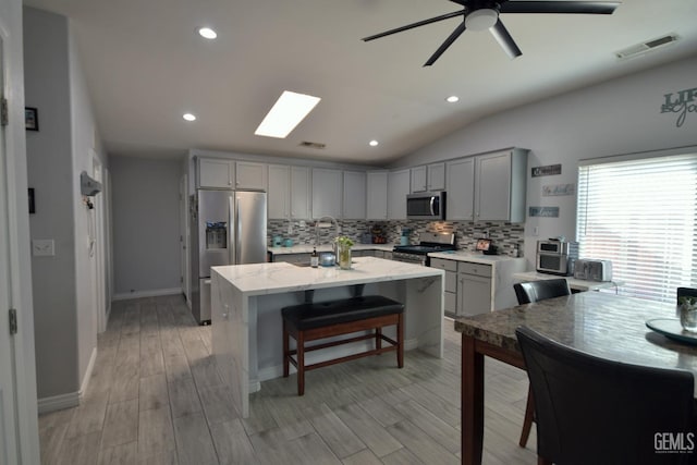 kitchen featuring appliances with stainless steel finishes, light wood-type flooring, backsplash, light stone counters, and gray cabinets