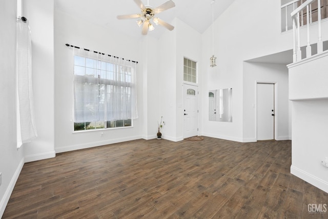 unfurnished living room with dark wood-type flooring, a towering ceiling, and ceiling fan