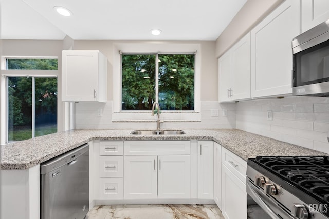 kitchen featuring sink, light stone counters, stainless steel appliances, kitchen peninsula, and white cabinets