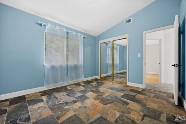 unfurnished bedroom featuring multiple windows, lofted ceiling, and a closet