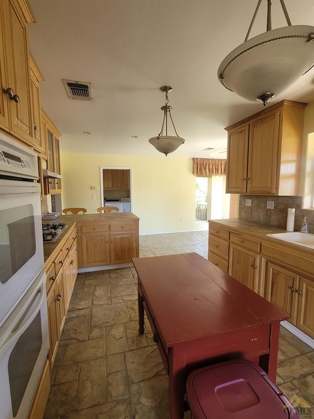 kitchen featuring white double oven, sink, hanging light fixtures, stainless steel gas cooktop, and tasteful backsplash