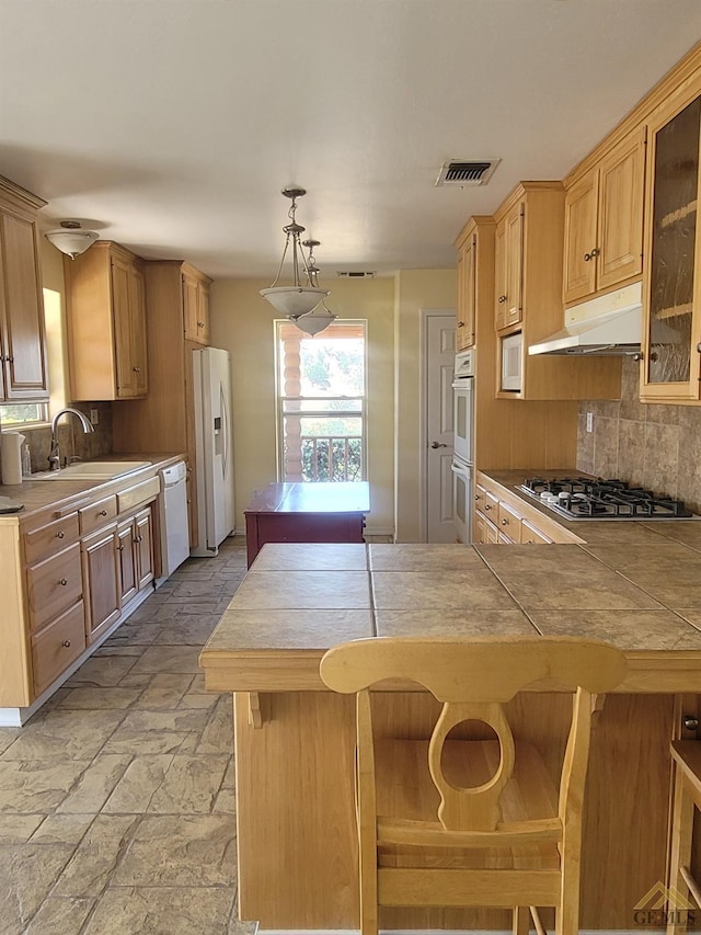 kitchen featuring white appliances, backsplash, hanging light fixtures, a kitchen bar, and kitchen peninsula