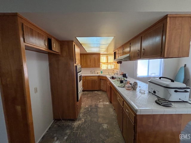 2710 Maher Way, Bakersfield, CA 93312 - kitchen featuring under cabinet range hood, dark stone finish floors, oven, tile countertops, and brown cabinets
