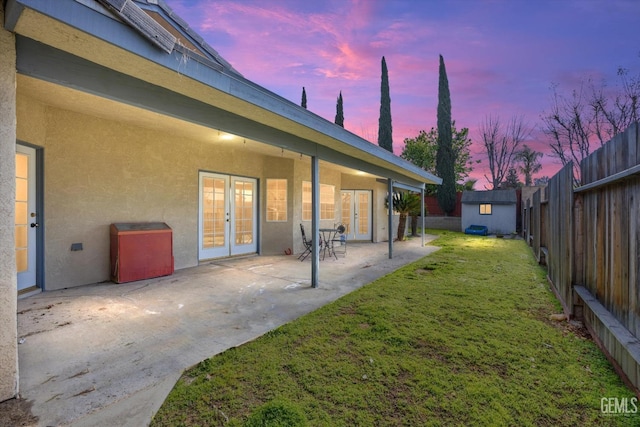 yard at dusk featuring a fenced backyard, an outbuilding, french doors, a patio area, and a shed