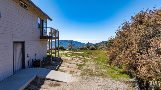 view of yard with a mountain view, central AC unit, and a balcony