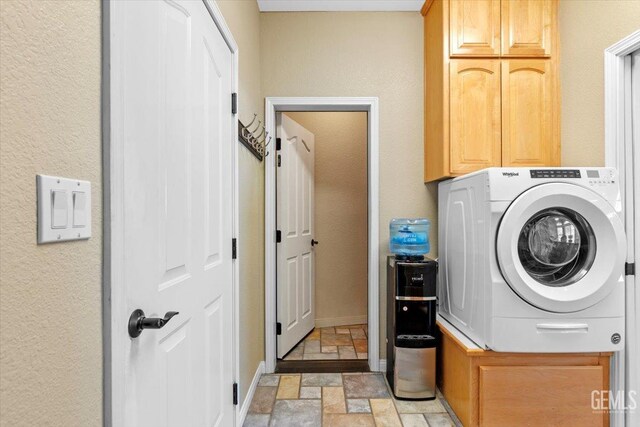 washroom with washer / dryer, a textured wall, cabinet space, and stone tile floors
