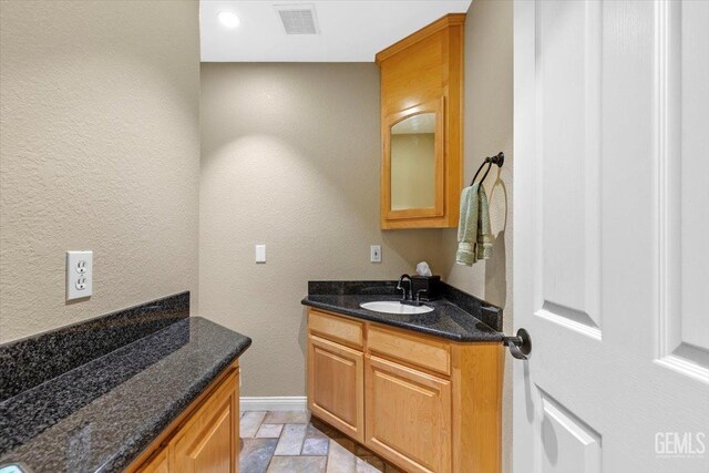bathroom with vanity, a textured wall, visible vents, and stone finish floor