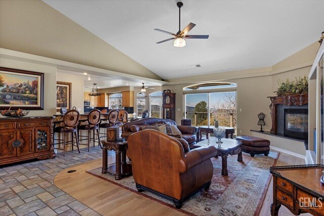 living room featuring a glass covered fireplace, high vaulted ceiling, and ceiling fan