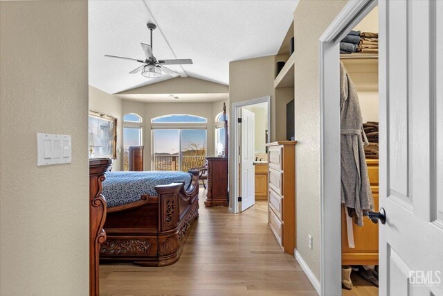 bedroom featuring a textured wall, vaulted ceiling, and light wood-style flooring