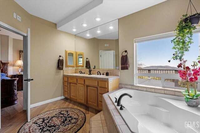 bathroom featuring double vanity, a bath, wood finished floors, and a sink
