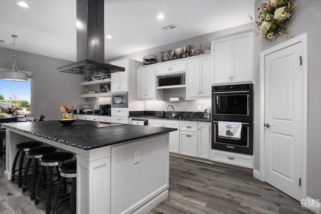 kitchen featuring built in microwave, double oven, a kitchen island, white cabinetry, and island exhaust hood