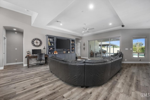 living room with a tray ceiling, ceiling fan, and wood-type flooring