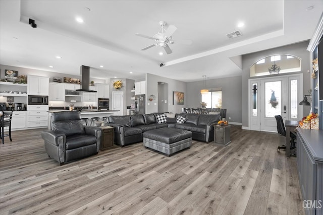 living room with a tray ceiling, ceiling fan, and light hardwood / wood-style floors