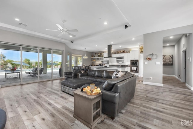 living room featuring ceiling fan, a tray ceiling, and light hardwood / wood-style flooring