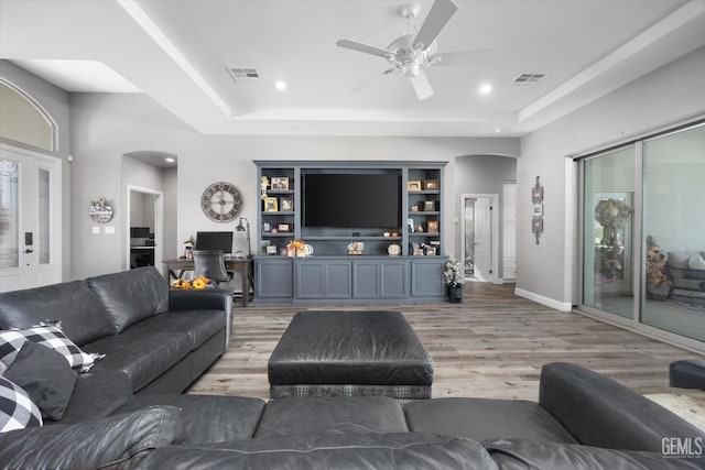 living room featuring a raised ceiling, ceiling fan, built in features, and wood-type flooring