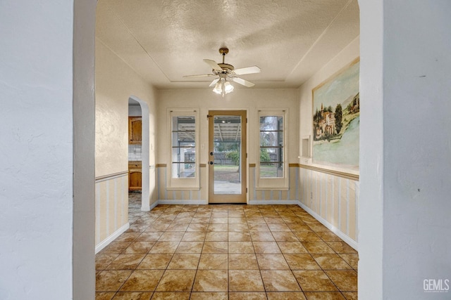 doorway with ceiling fan, light tile patterned floors, and a textured ceiling