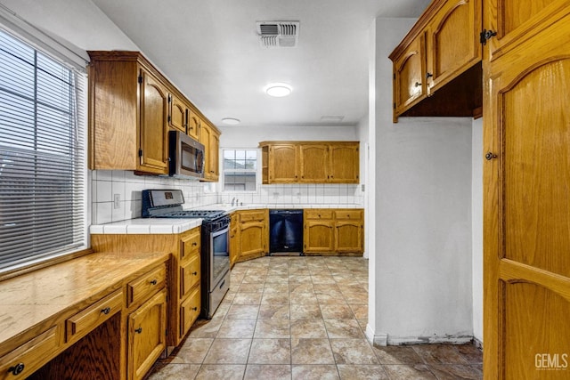 kitchen with light tile patterned floors, tasteful backsplash, stainless steel appliances, and tile counters