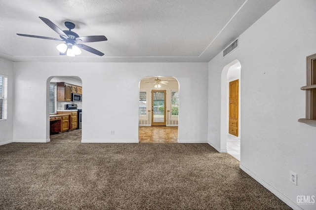 carpeted spare room featuring a wealth of natural light, ceiling fan, and a textured ceiling