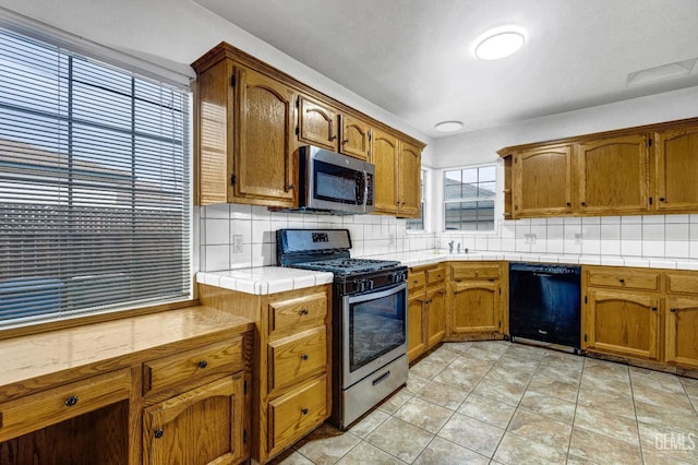 kitchen featuring appliances with stainless steel finishes, light tile patterned flooring, tasteful backsplash, and tile counters