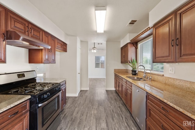 kitchen with ceiling fan, sink, stainless steel appliances, light stone counters, and dark hardwood / wood-style flooring