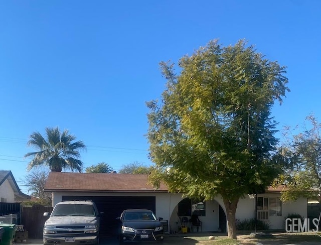 view of front of house with driveway, an attached garage, fence, and stucco siding