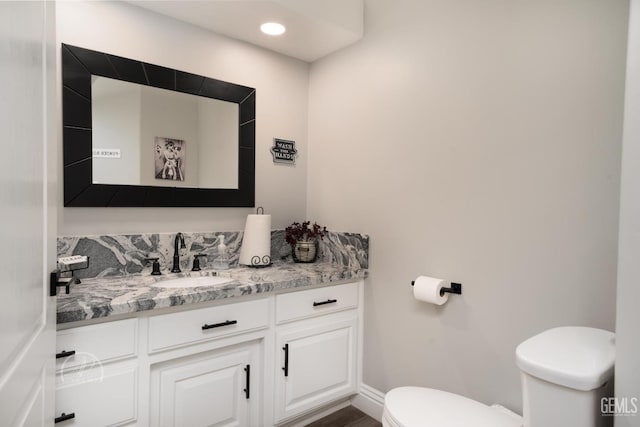 half bathroom with recessed lighting, baseboards, vanity, and toilet