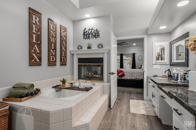 bathroom featuring ensuite bathroom, a fireplace, wood finished floors, vanity, and a bath