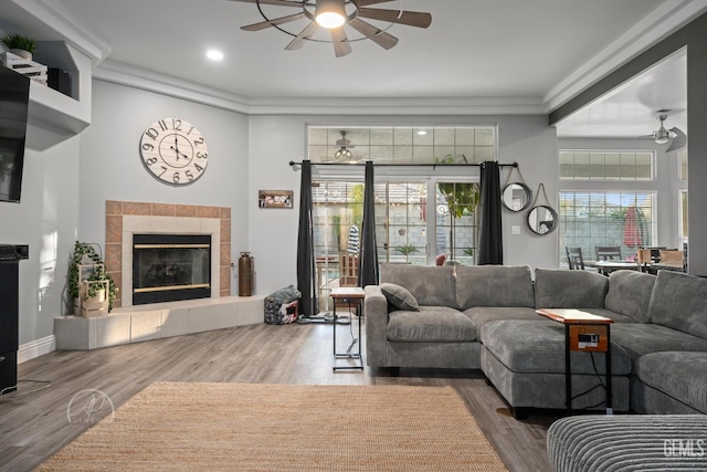 living room with a tile fireplace, wood finished floors, crown molding, and ceiling fan