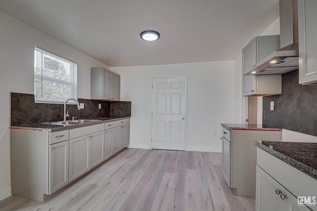 kitchen featuring gray cabinetry, sink, wall chimney range hood, light hardwood / wood-style flooring, and decorative backsplash