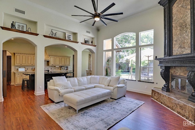1881 Richert Ave, Clovis, CA 93611 - living room featuring a ceiling fan, a towering ceiling, crown molding, dark wood-style floors, and a stone fireplace