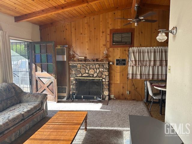 living room featuring carpet flooring, ceiling fan, a fireplace, vaulted ceiling with beams, and wood walls