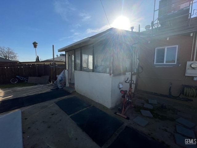 view of property exterior with a patio area, fence, and a sunroom