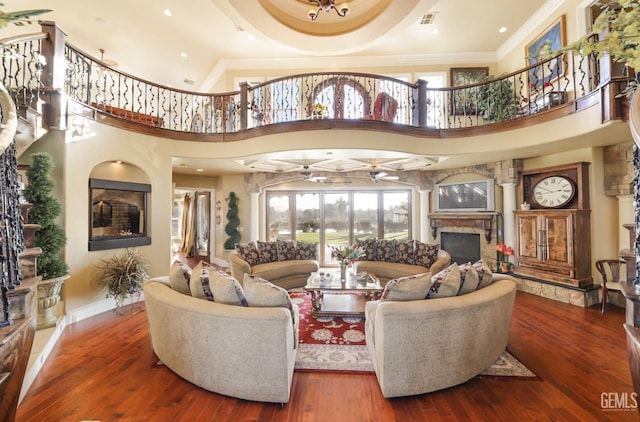 living room with ceiling fan, a high ceiling, hardwood / wood-style flooring, a stone fireplace, and ornamental molding