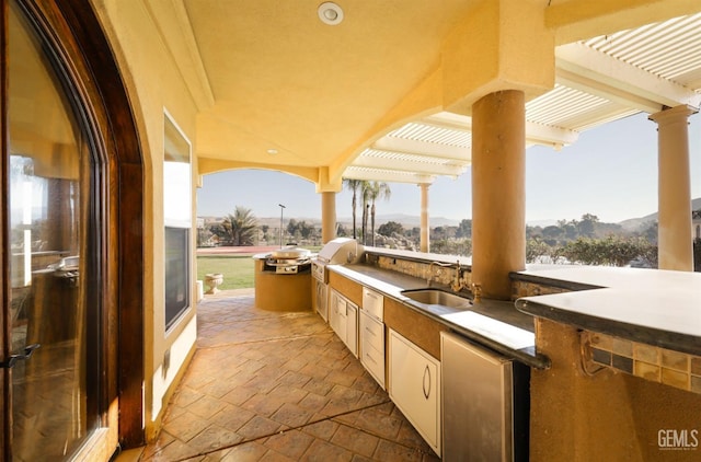 view of patio featuring exterior kitchen, sink, a mountain view, grilling area, and a pergola