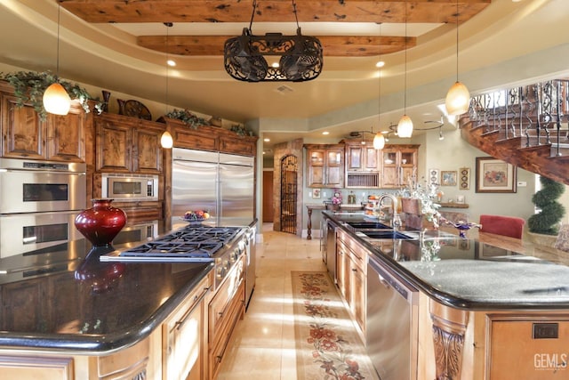 kitchen with a raised ceiling, an island with sink, sink, and built in appliances