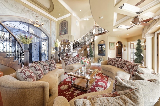 living room with a towering ceiling, ceiling fan with notable chandelier, ornamental molding, and ornate columns