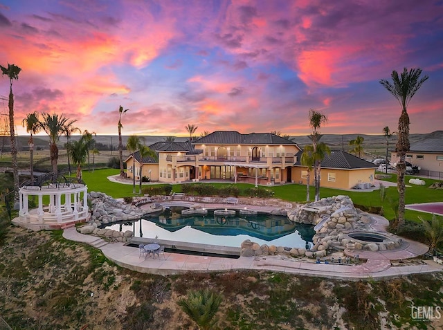 pool at dusk with an in ground hot tub, a lawn, and a patio