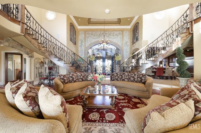 living room featuring an inviting chandelier, decorative columns, a high ceiling, a tray ceiling, and ornamental molding