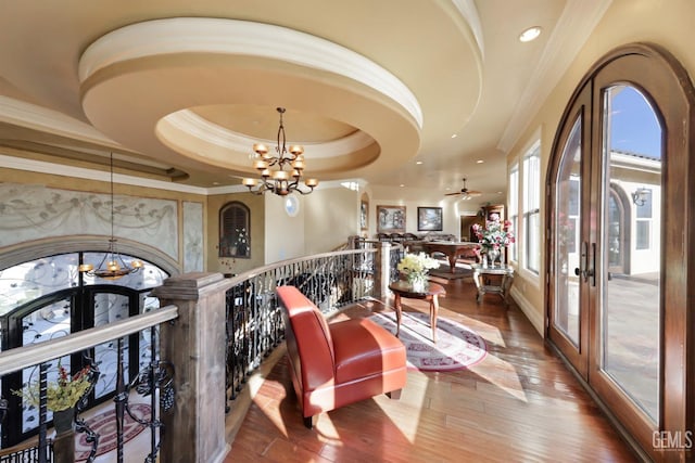 corridor featuring wood-type flooring, french doors, a tray ceiling, and a notable chandelier