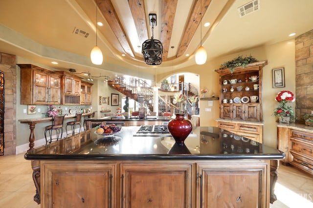 kitchen with light tile patterned floors, beam ceiling, a center island, and decorative light fixtures