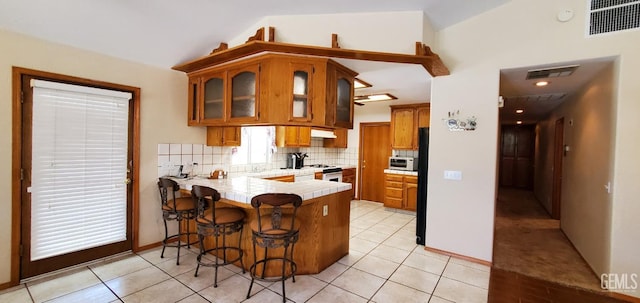 kitchen featuring kitchen peninsula, decorative backsplash, a breakfast bar, white appliances, and lofted ceiling