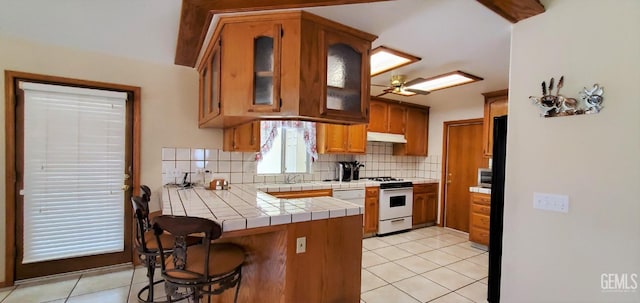 kitchen featuring tile counters, white range, backsplash, kitchen peninsula, and light tile patterned flooring