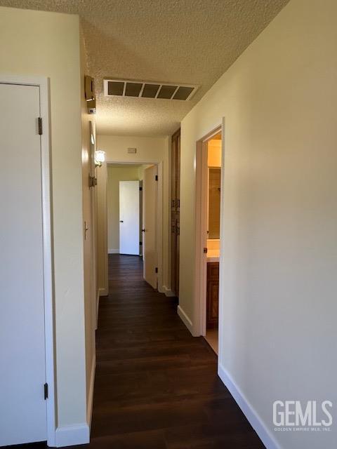 corridor featuring dark wood finished floors, visible vents, a textured ceiling, and baseboards