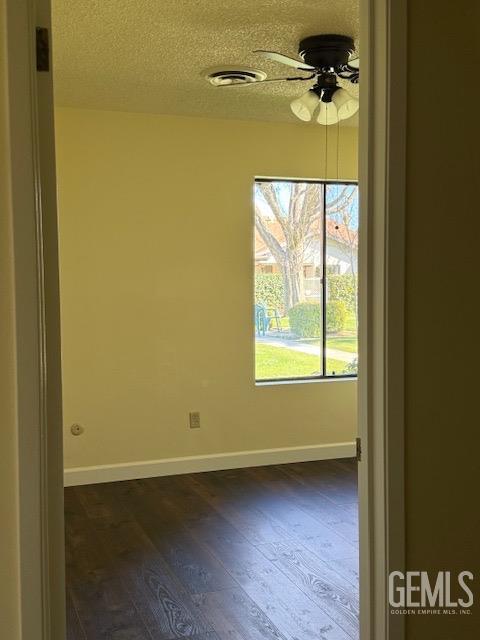 spare room featuring dark wood finished floors, baseboards, visible vents, and a textured ceiling