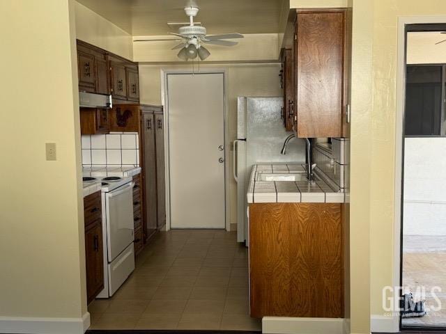 kitchen featuring under cabinet range hood, tile countertops, white appliances, decorative backsplash, and ceiling fan