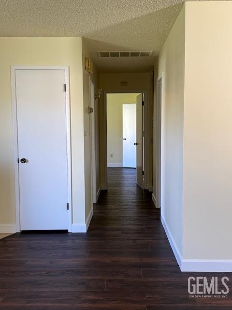 corridor featuring baseboards, dark wood-style floors, visible vents, and a textured ceiling